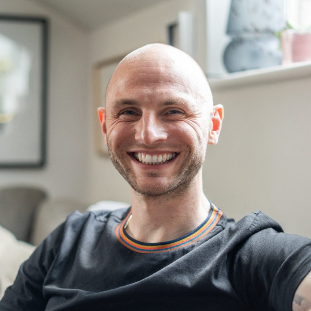 A photo of Dan Godley on a sofa, smiling at the camera.