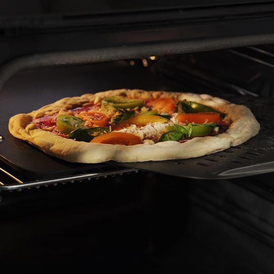 Pysznie wyglądająca pizza wkładana do czarnego piekarnika