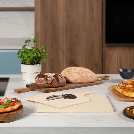 Zestaw do pizzy: kamień, drewniana łoptaka i nóż do krojenia pizzy na blacie wśród wypieków